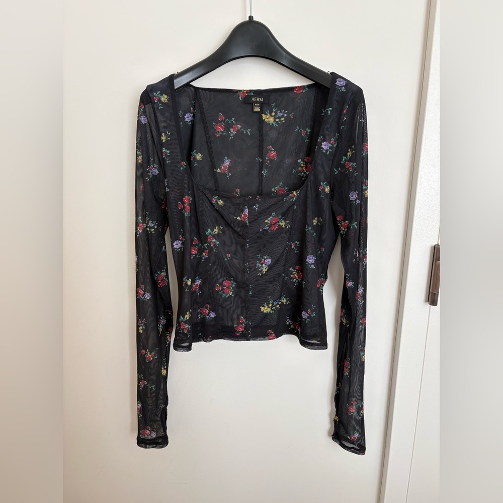 Black partially sheer long sleeve top with floral pattern. Comfortable, stretchy